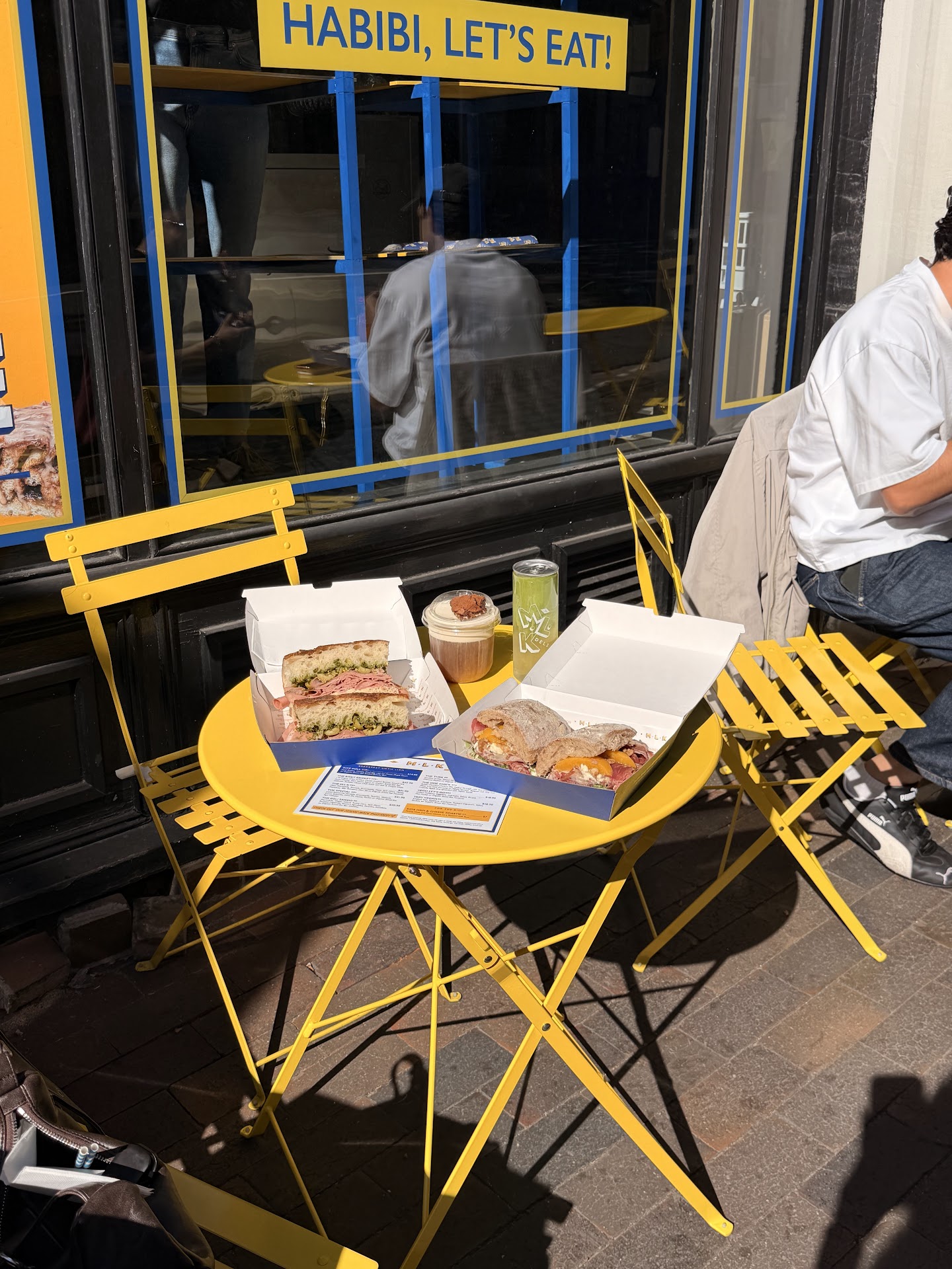 Outdoor yellow table with MLK Deli sandwiches and drinks