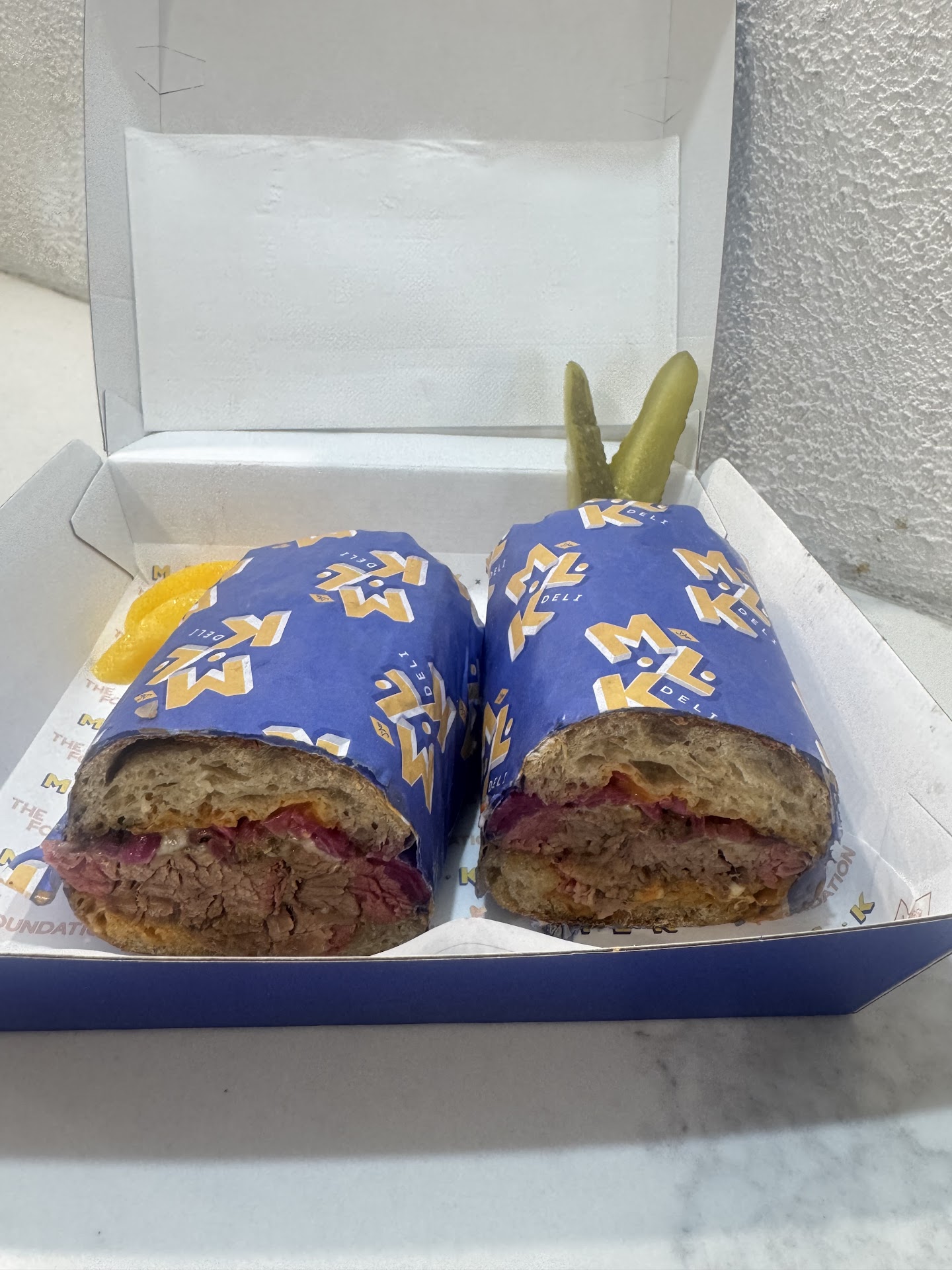 Two wrapped brisket sandwich halves with pickles