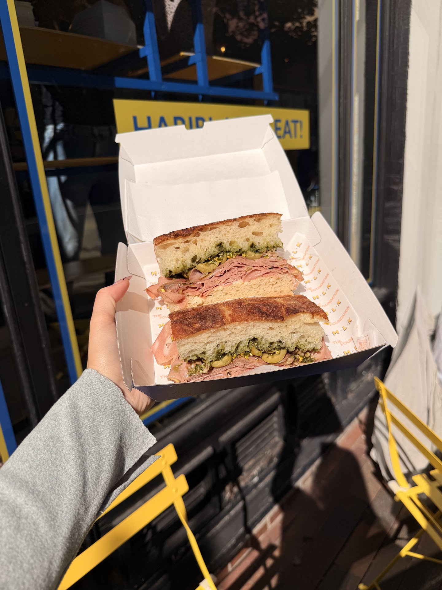 A stacked MLK Deli sandwich held outside the Harrington Street shopfront